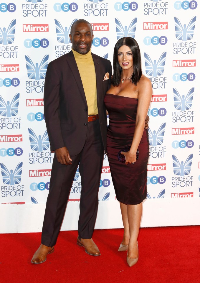 a man and woman pose on a red carpet in front of a wall that says pride of sport