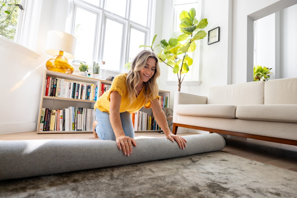 a woman in a yellow shirt is rolling a rug in a living room