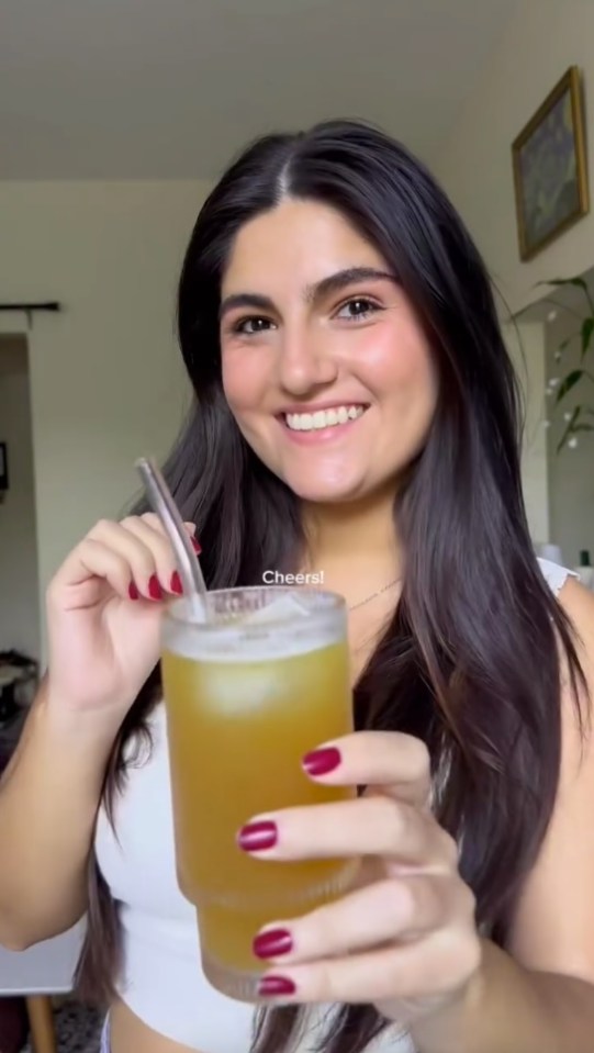 a woman with red nails is holding a glass of liquid with a straw