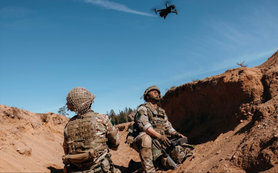 two soldiers looking up at a drone in the sky