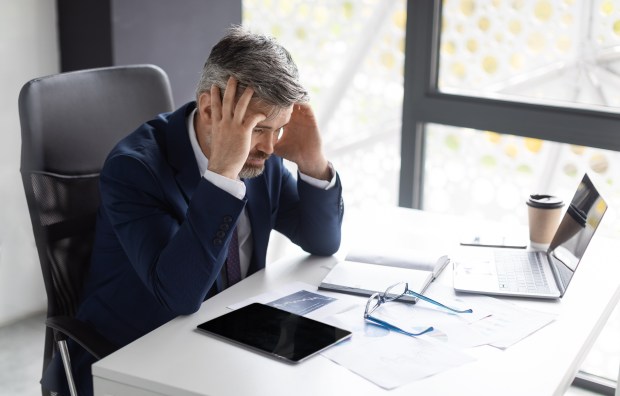 a man in a suit sits at a desk with his hands on his head