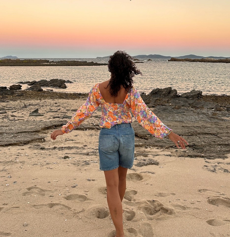 a woman in a floral top and shorts is walking on the beach