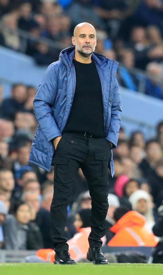 a bald man wearing a blue jacket and black pants stands on a soccer field