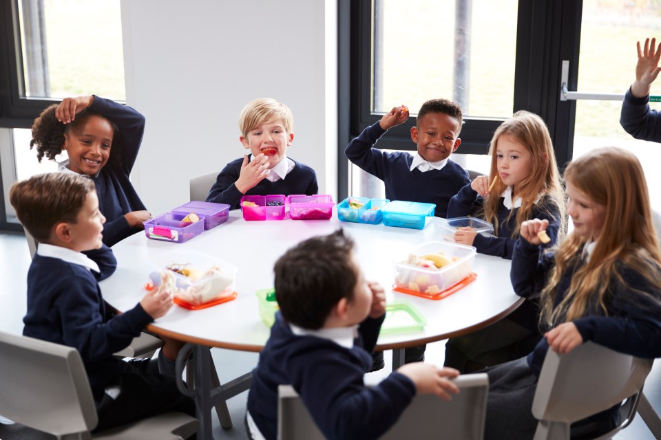 a group of children are sitting around a table eating lunch