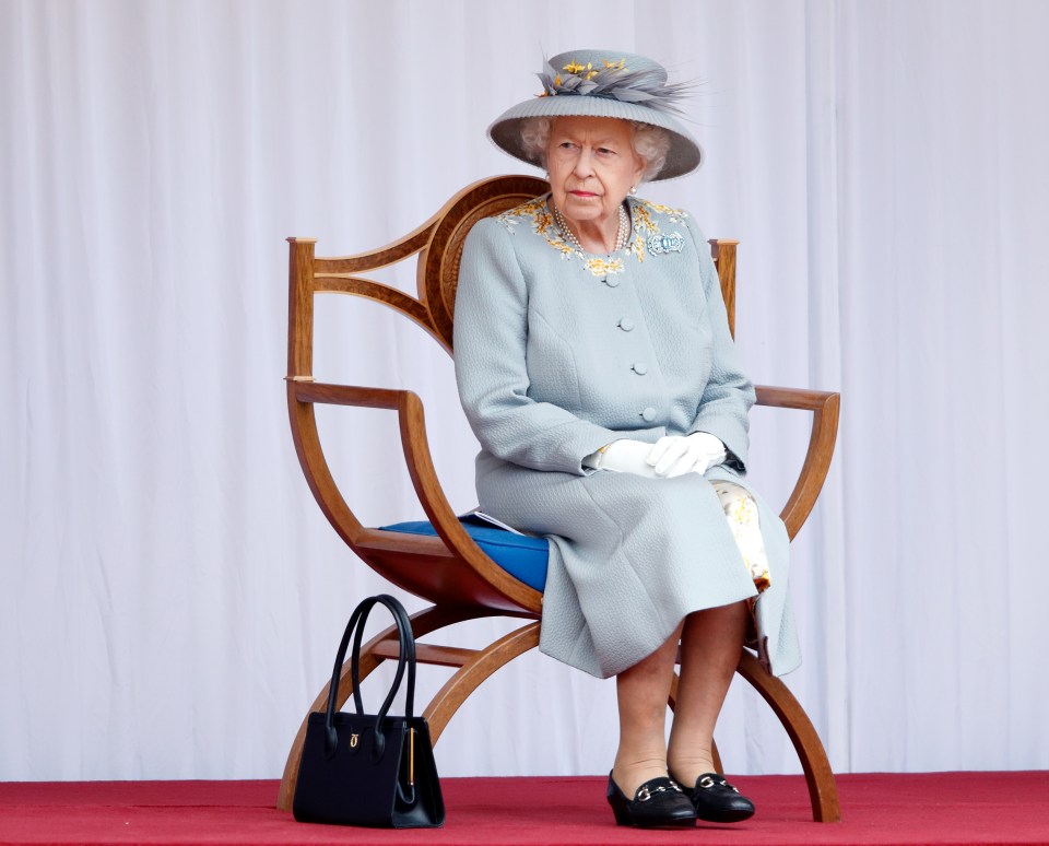 queen elizabeth ii sits in a chair with her hands folded