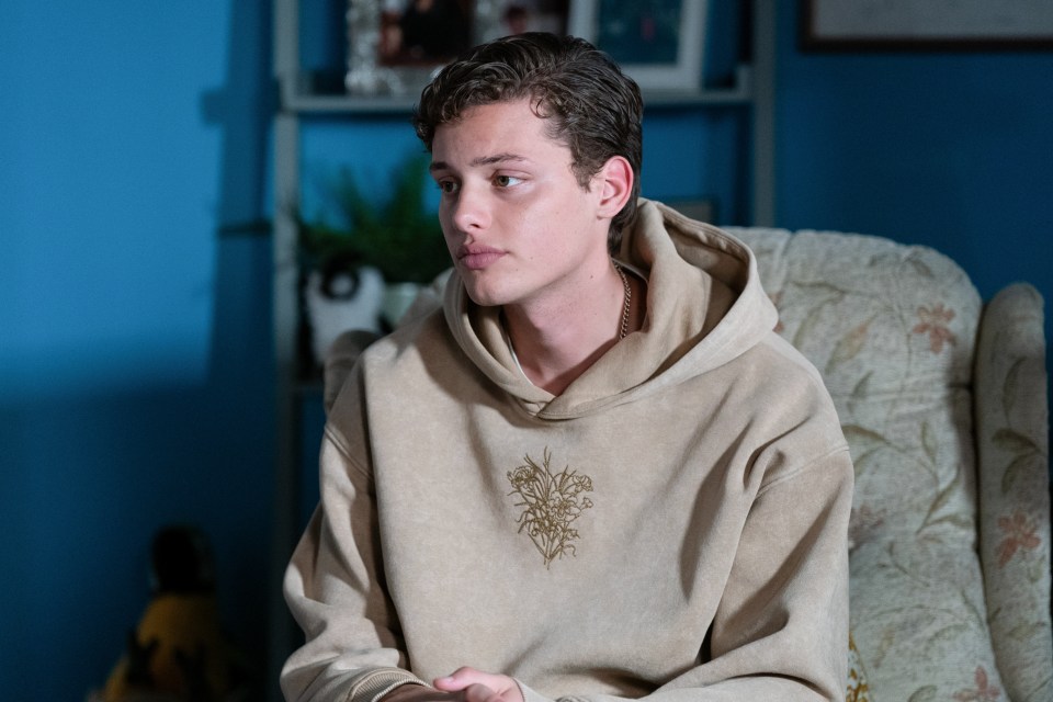 a young man in a tan hoodie sits in a chair