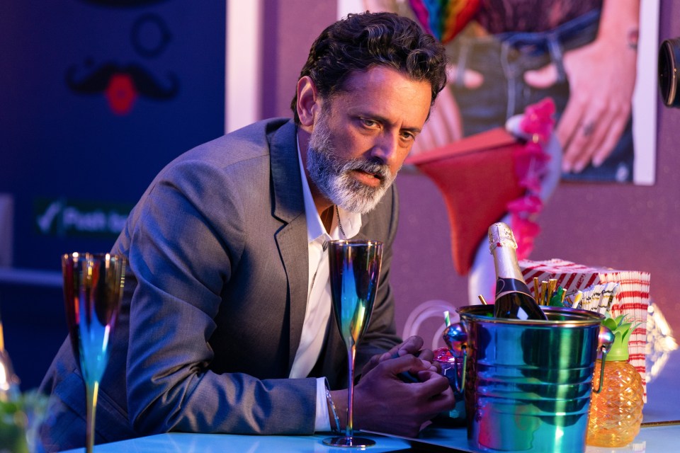 a man in a suit sits at a bar with a bottle of champagne in a bucket