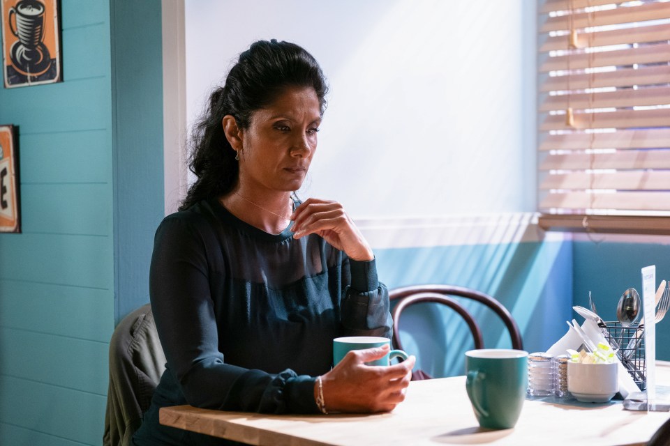 a woman sits at a table holding a cup of coffee