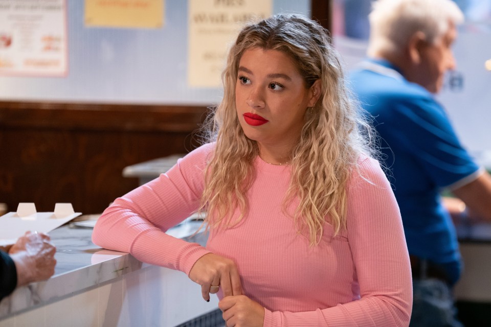 a woman in a pink shirt is leaning on a counter