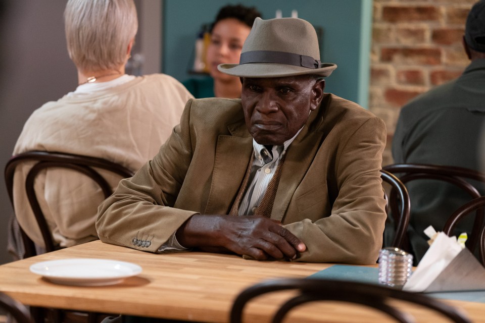 a man in a hat sits at a table with his hands folded