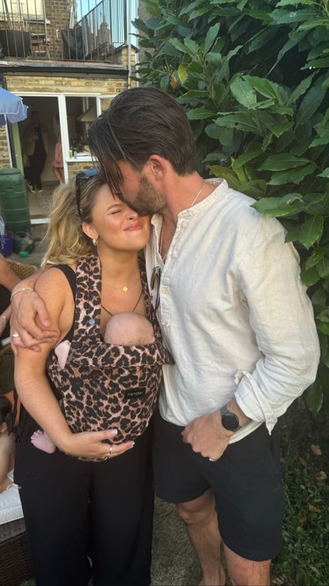 a man kisses a woman while holding a baby in a leopard print carrier