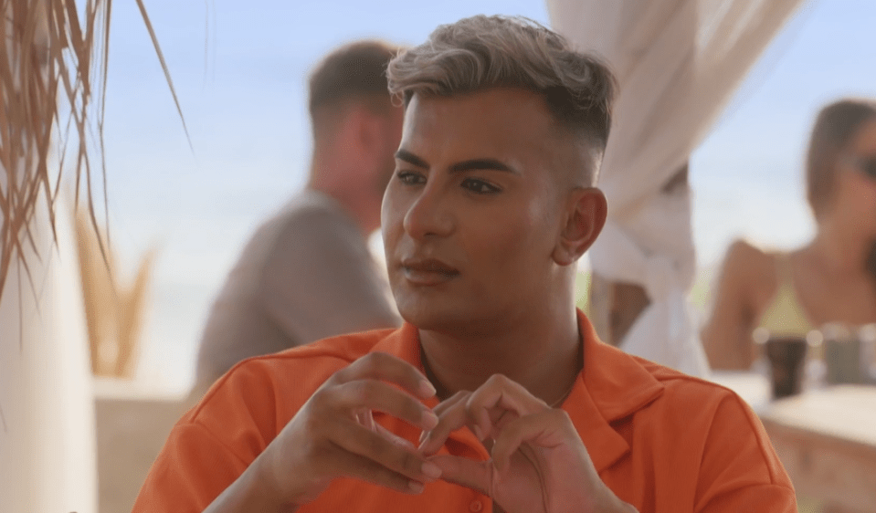 a man in an orange shirt is making a heart shape with his hands