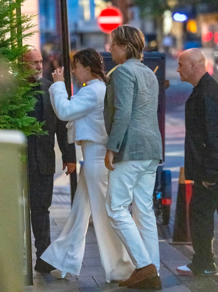 a man in a grey jacket stands next to a woman in white pants