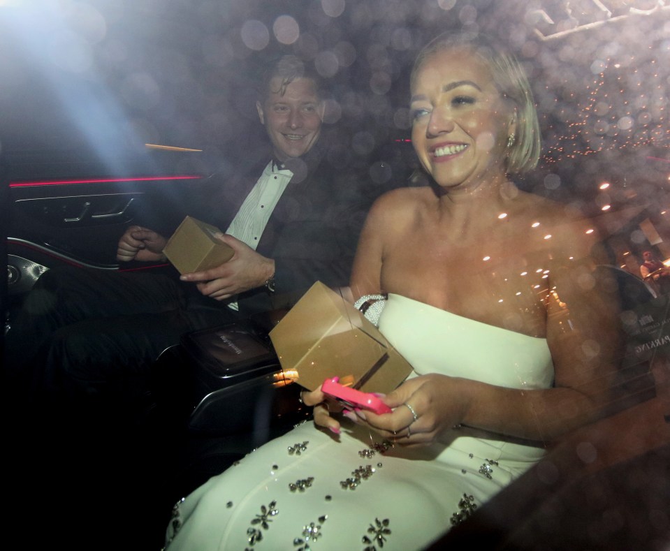 a man in a tuxedo holds a cardboard box and a woman in a white dress holds a cell phone