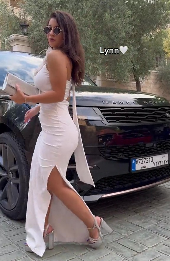 a woman in a white dress stands in front of a black range rover