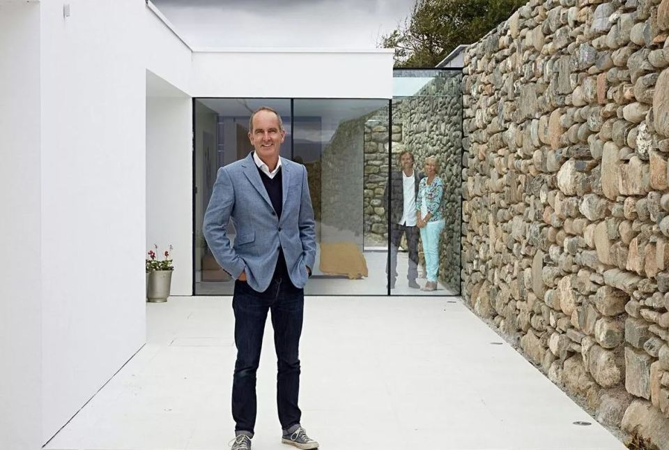 a man in a blue suit stands in front of a stone wall