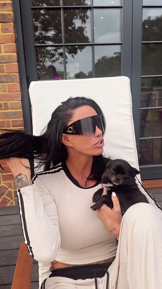 a woman wearing sunglasses holds a small black dog