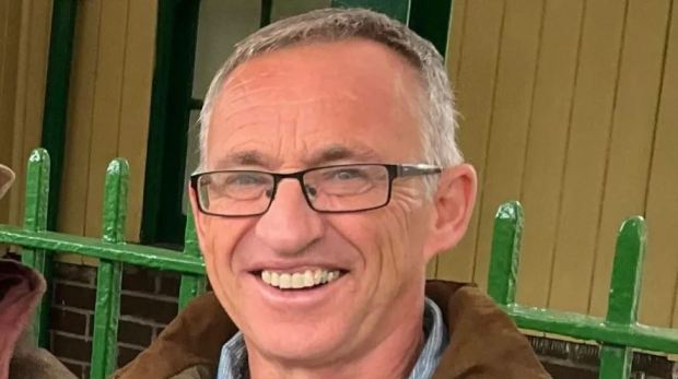 a man wearing glasses is smiling in front of a green fence