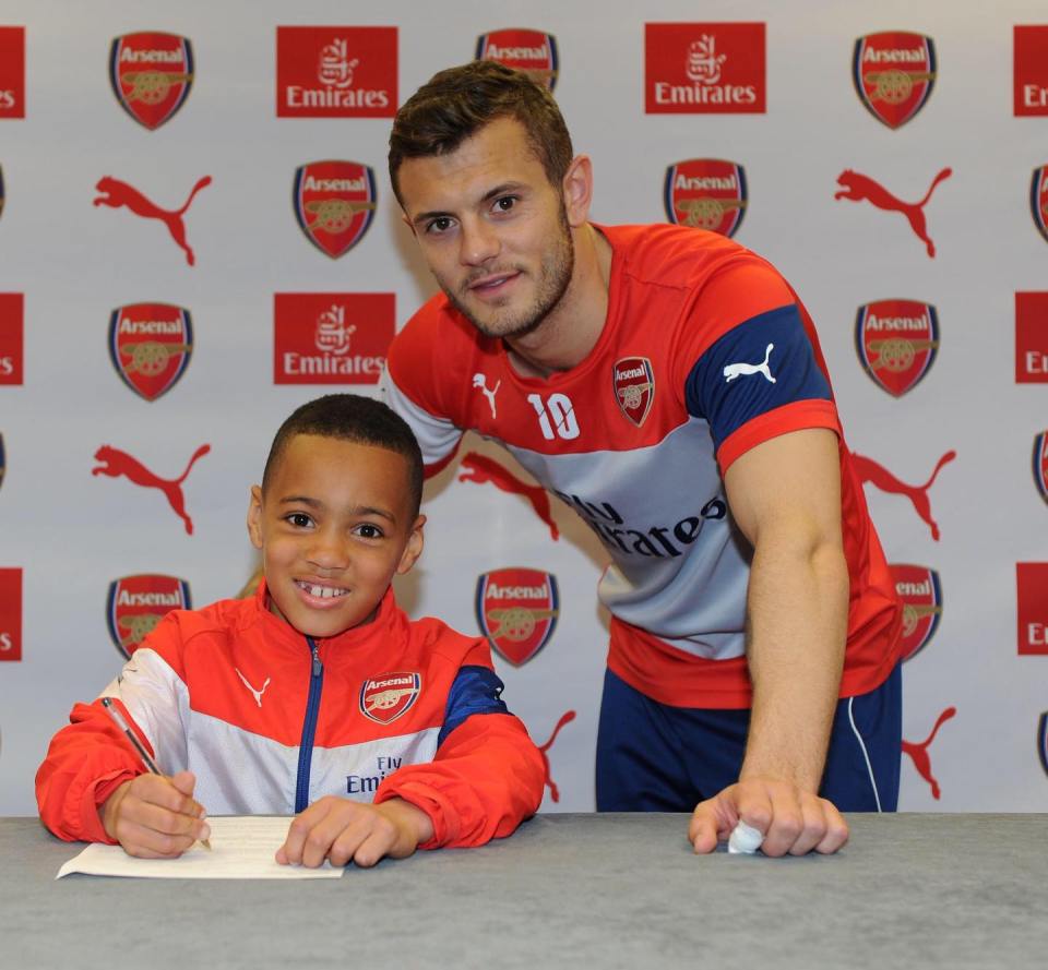 two soccer players are posing for a picture in front of a wall with arsenal and emirates logos