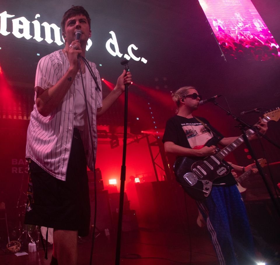 a man singing into a microphone in front of a sign that says tain d.c.