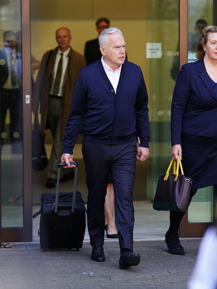 a man carrying a suitcase and a woman carrying a purse walks out of a building