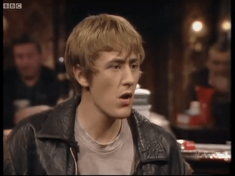 a man in a leather jacket is sitting at a table in a bar .