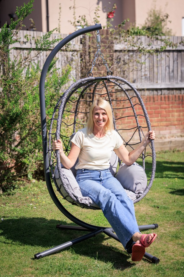 a woman is sitting in a hanging chair in the grass