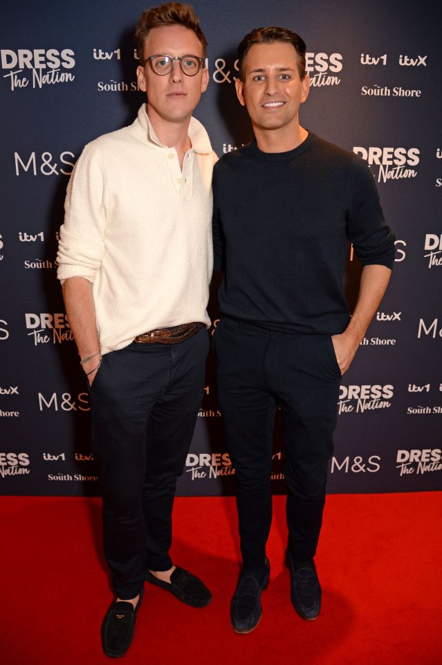 two men stand on a red carpet in front of a sign that says dress the nation