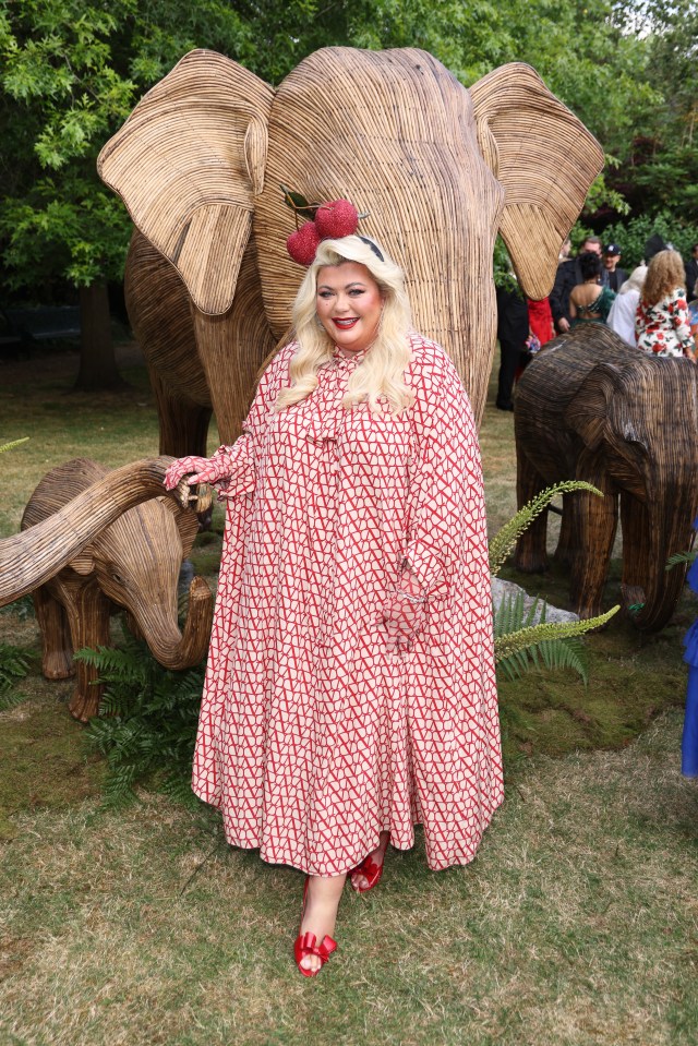 a woman in a red and white dress stands in front of a large elephant statue