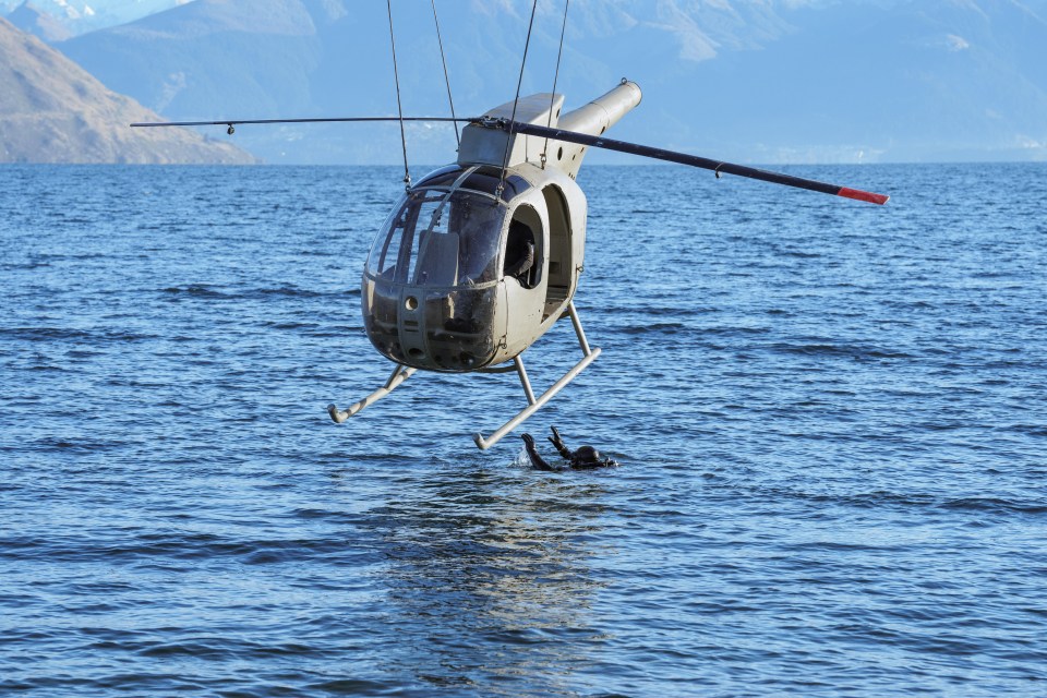 a helicopter is flying over a body of water with mountains in the background