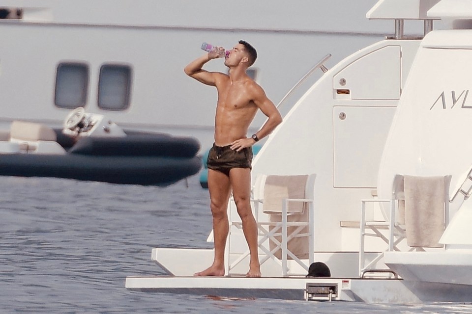 a shirtless man drinks from a bottle while standing on a boat that says avl