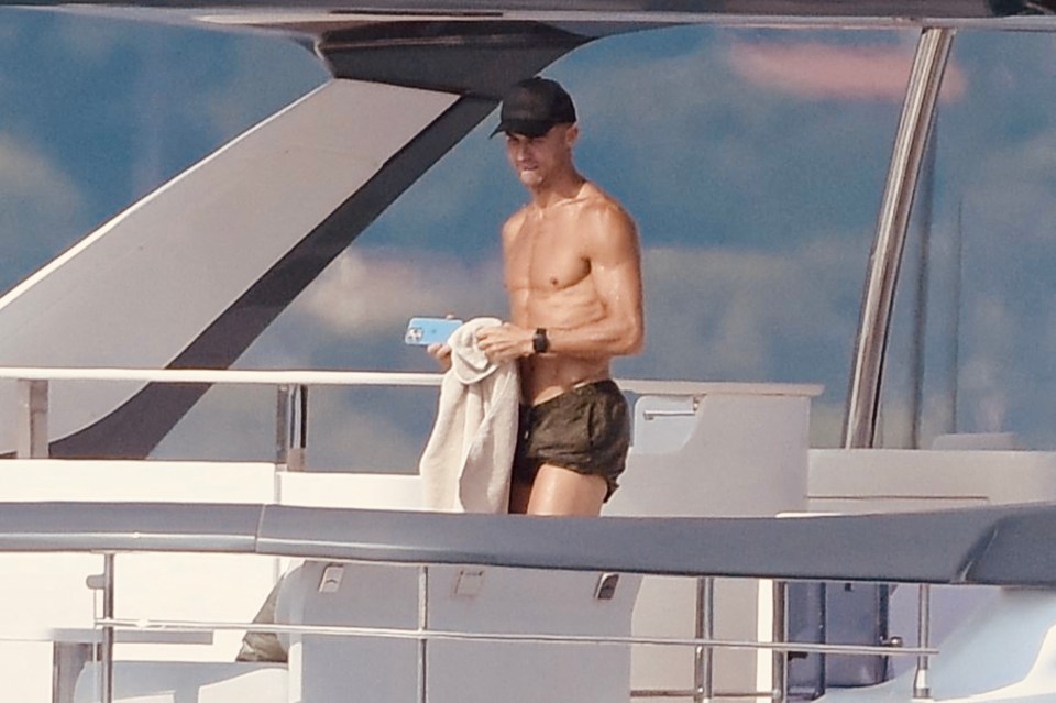 a shirtless man standing on a boat holding a towel