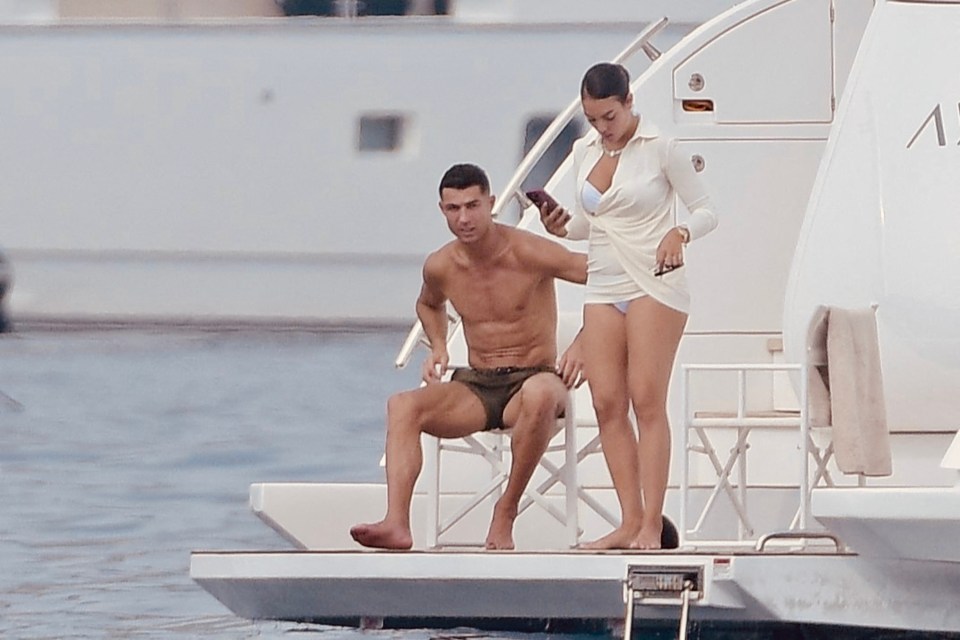 a shirtless man sits on a chair while a woman looks at her phone