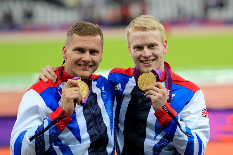 two athletes holding up their gold medals one of whom is wearing an adidas jacket