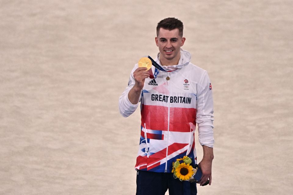 a man in a great britain jacket holds up his gold medal