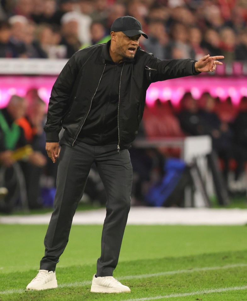 a man in a black jacket and white shoes stands on a soccer field