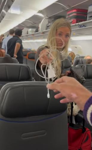 a woman is sitting on an airplane holding a charging cord .