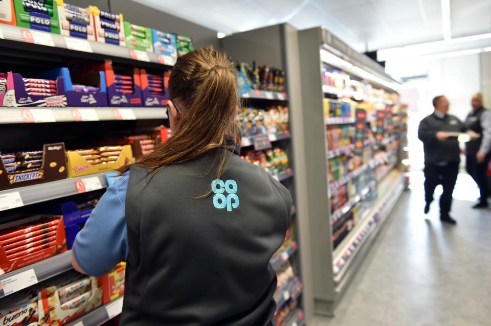 a woman wearing a co op vest is standing in a grocery store