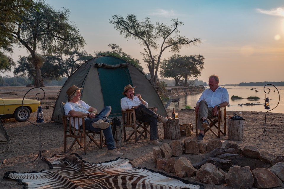 three men sit around a campfire in front of a tent