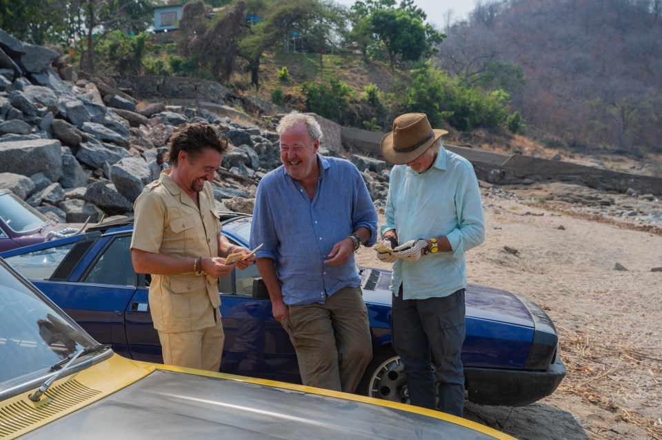 three men standing next to a blue car on a beach