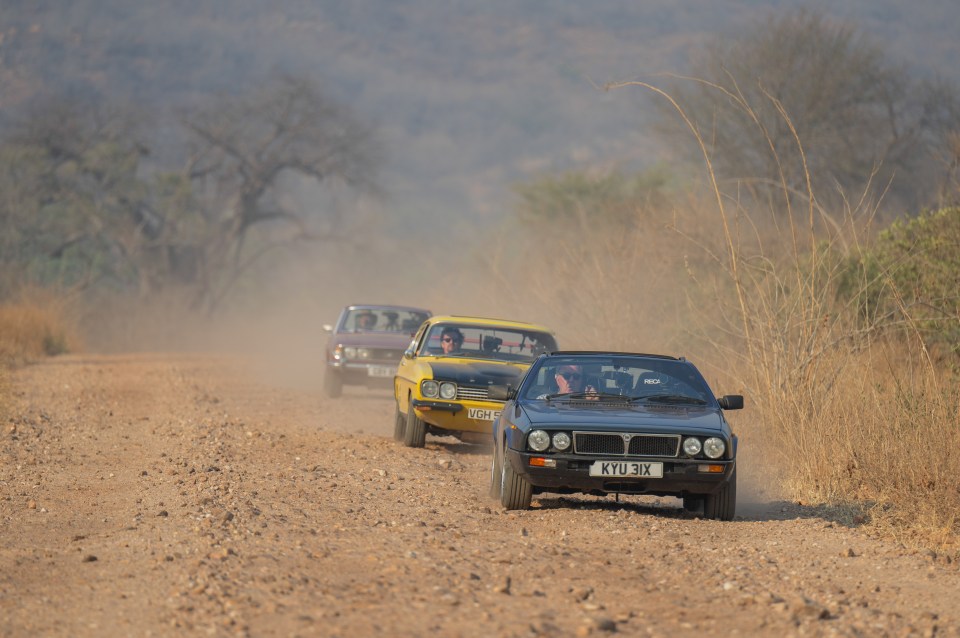 a row of cars are driving down a dirt road and one has a license plate that says kyu-ix