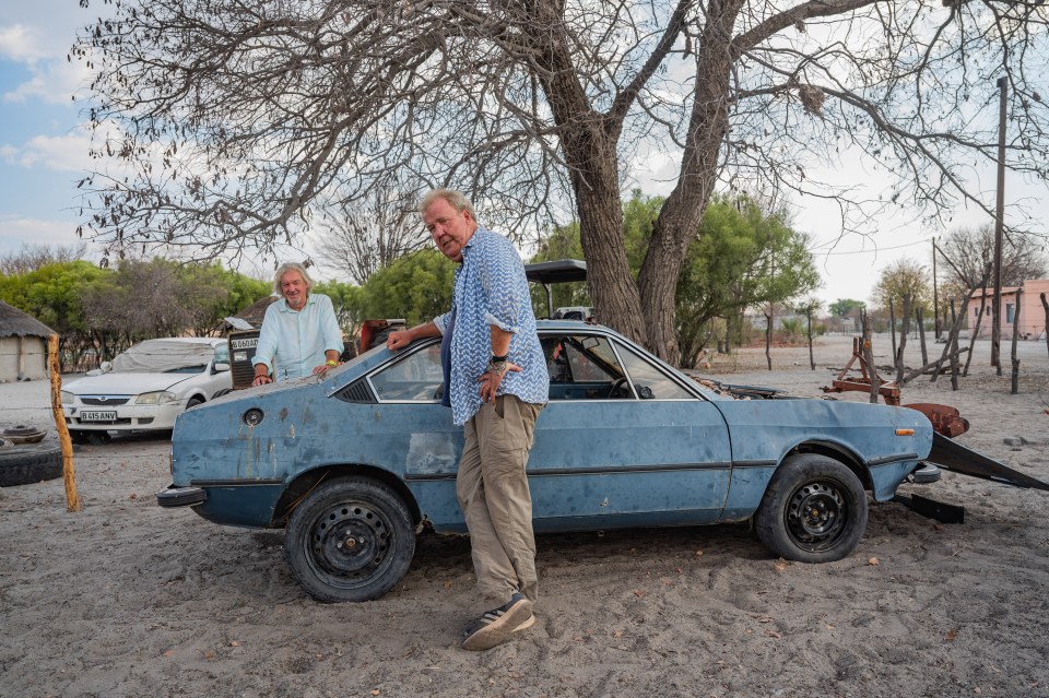 two men are standing next to a blue car with a flat tire