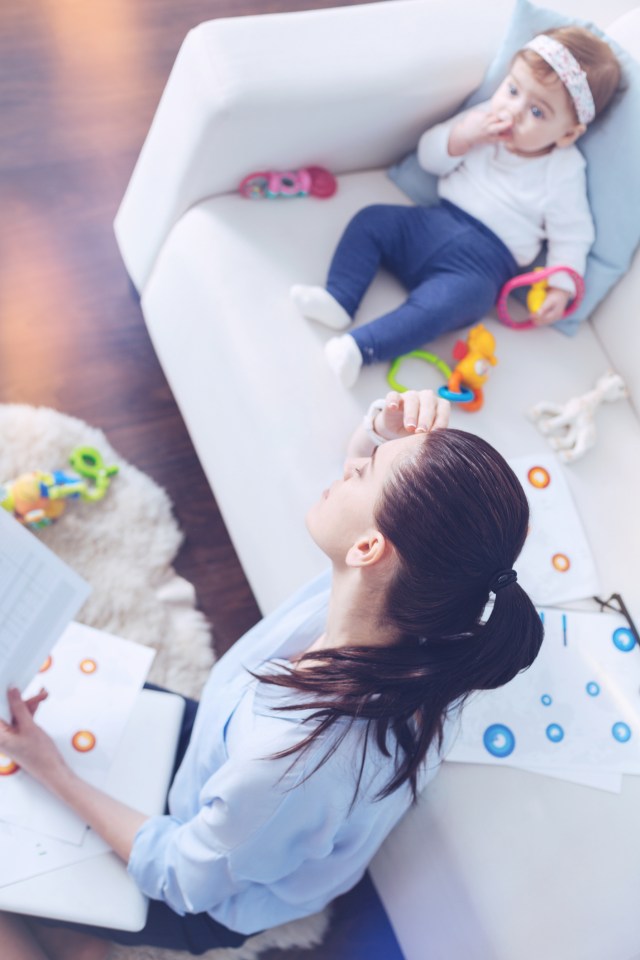 a woman sits on a couch with a baby and a laptop