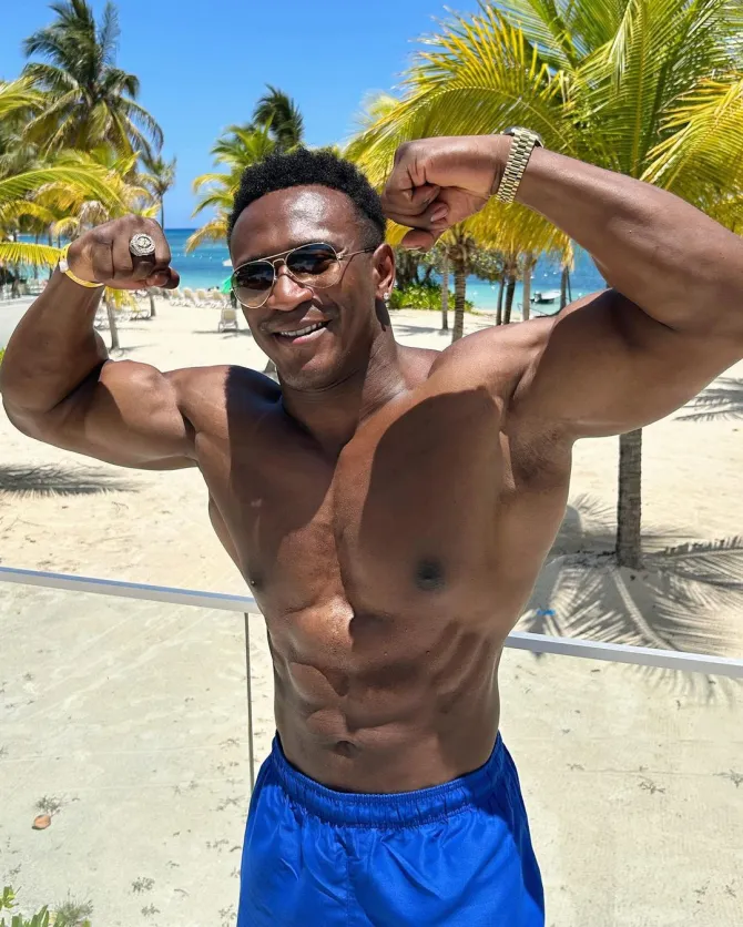 a shirtless man flexes his muscles on the beach