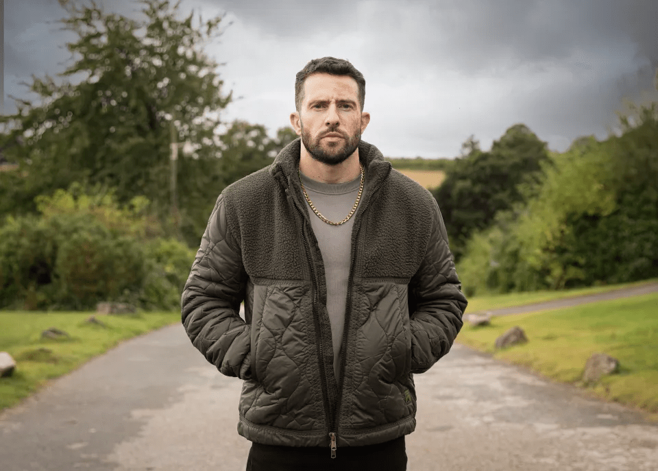 a man with a beard is wearing a jacket and a chain around his neck