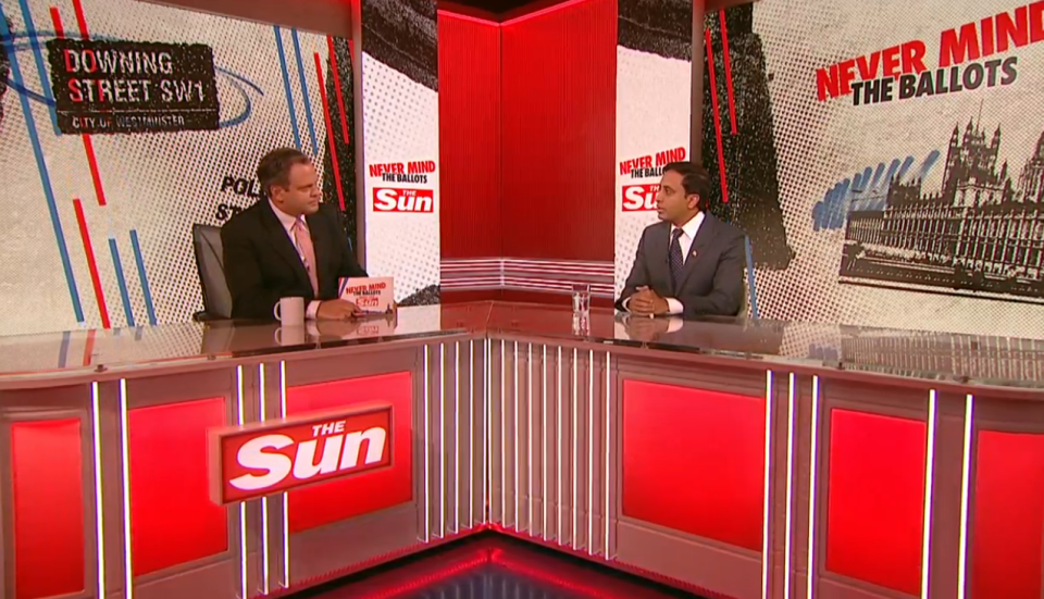 a man sits at a desk in front of a sign that says the sun