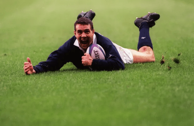 a man laying on the grass with a rugby ball that says ' gilbert ' on it