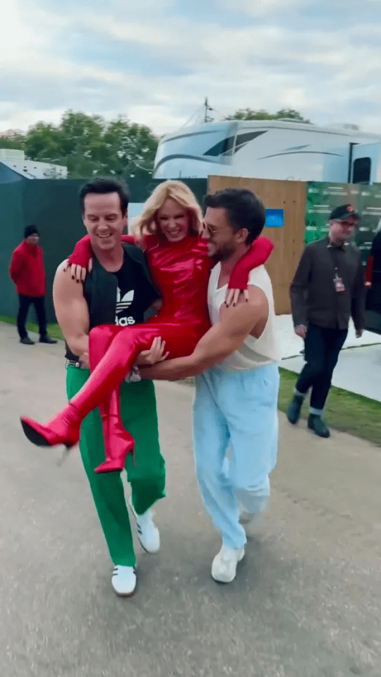 a man in a black adidas shirt is carrying a woman in red boots