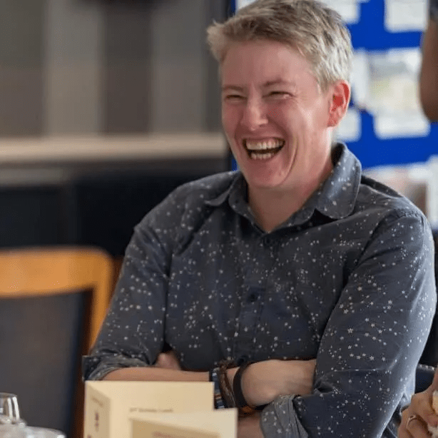 a woman is sitting at a table with her arms crossed and laughing .