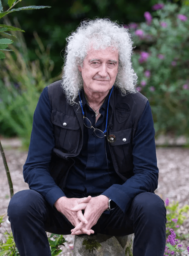 a man with curly hair sits on a rock with his hands folded